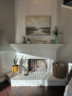 Lareira de tijolos brancos com um quadro acima, rodeada por diversos objetos decorativos.