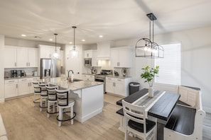 A modern kitchen with white cabinetry, a central island, bar stools, and pendant lighting.