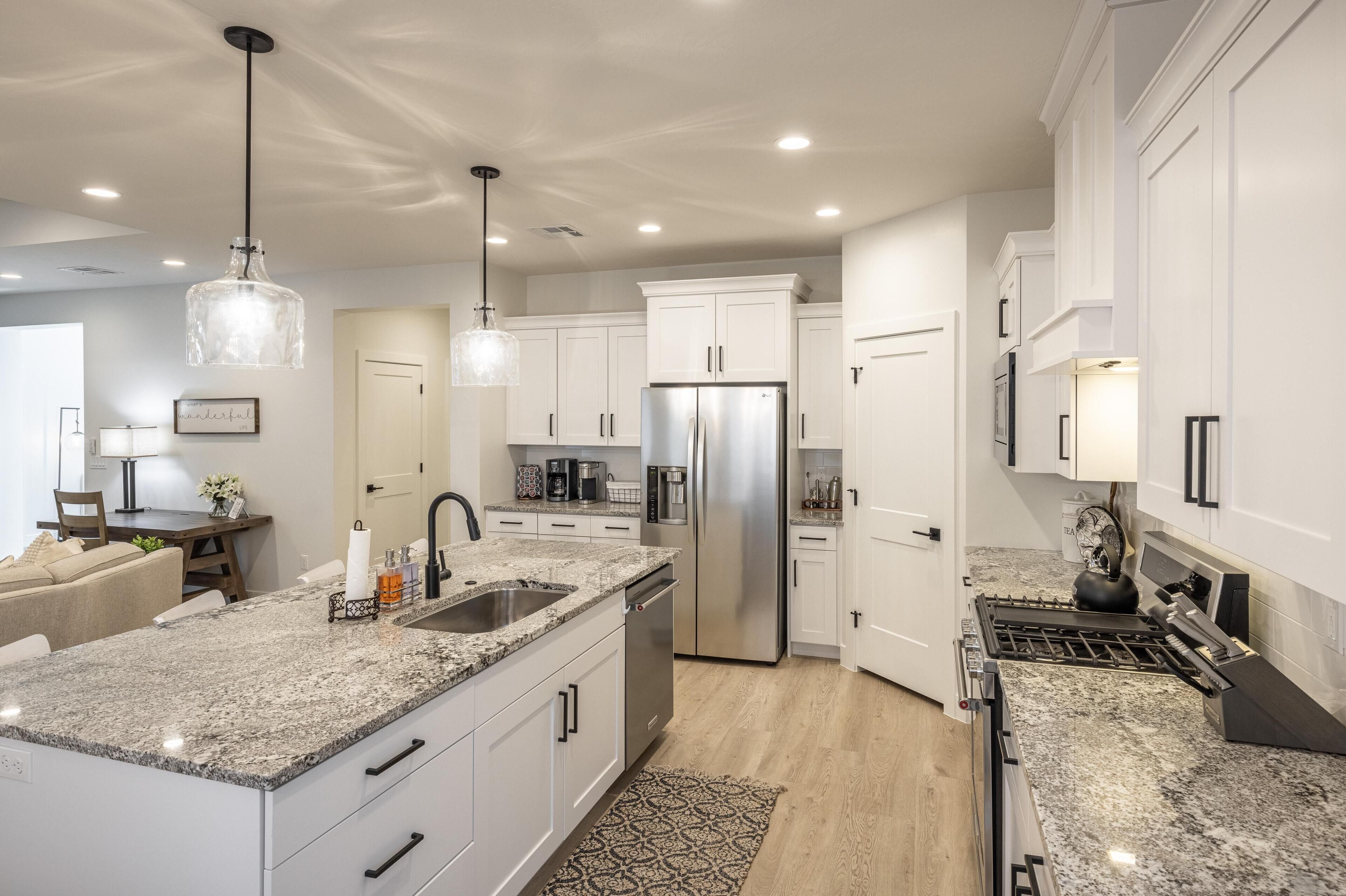 A modern kitchen with white cabinets, granite countertops, stainless steel appliances, and pendant lighting.