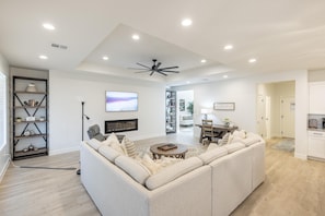 A modern living room with a sectional sofa, a coffee table, a ceiling fan, recessed lighting, a TV, and a bookshelf.