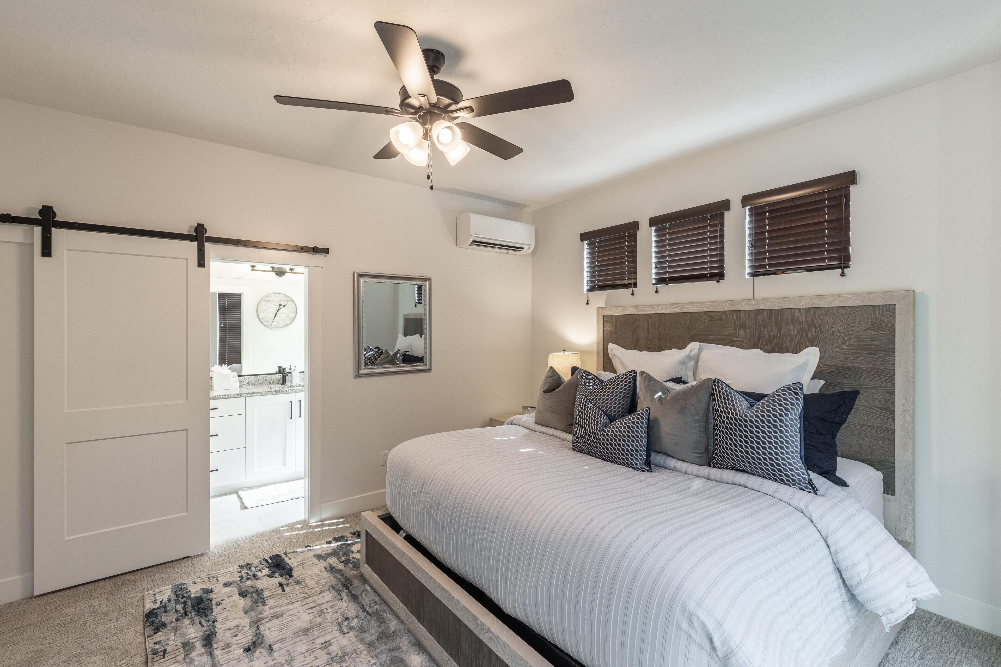 A bedroom with a bed, a ceiling fan, a window with blinds, and a door leading to a bathroom.