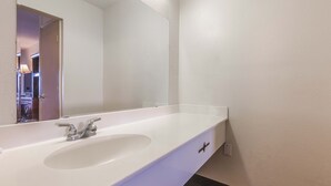 Un baño con un lavamanos blanco, un espejo y una puerta que da a otra habitación.
