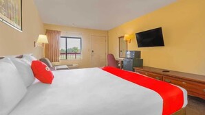 Habitación de hotel con cama, escritorio, silla, televisor y ventana con cortinas.