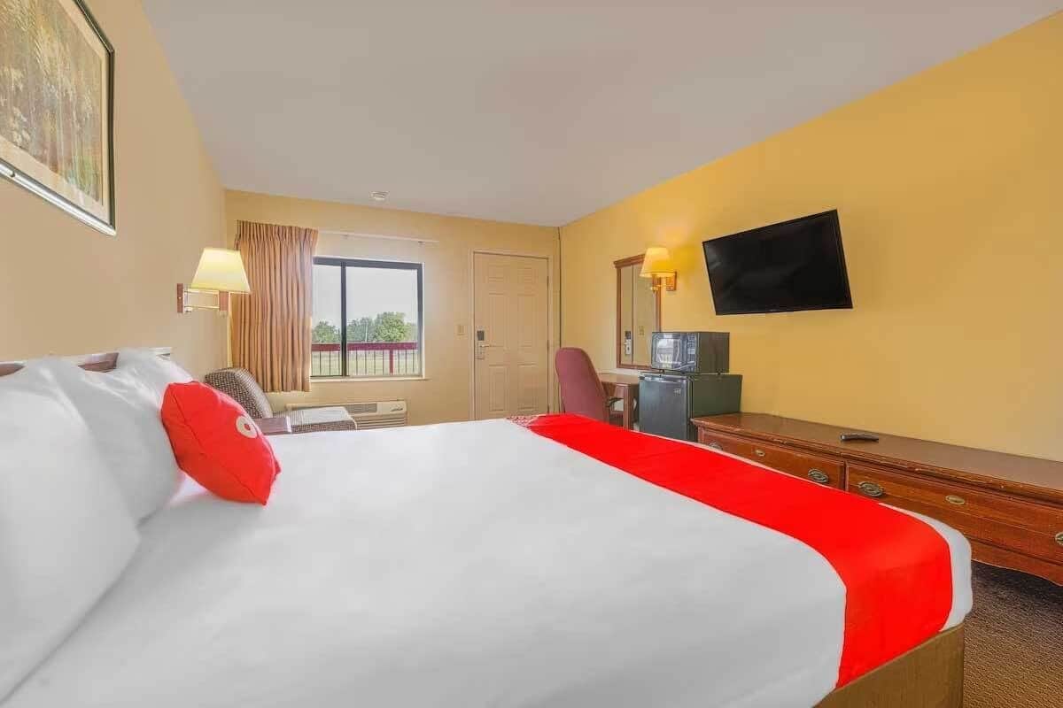 A hotel room with a bed, a desk, a chair, a television, and a window with curtains.