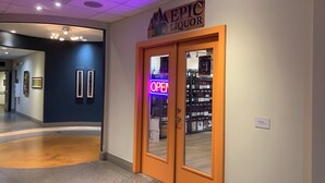 A hallway with a sign for 'EPIC LIQUOR' and a neon 'OPEN' sign on the door.
