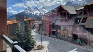 A mountain town with buildings featuring large windows and balconies, a paved street, and snow-capped mountains in the background.