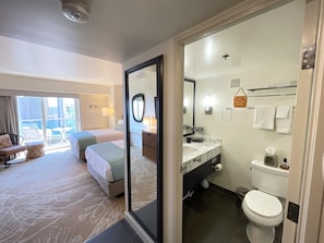 Ett hotellrum med en balkong, en säng, ett skrivbord och ett badrum med toalett och handfat.