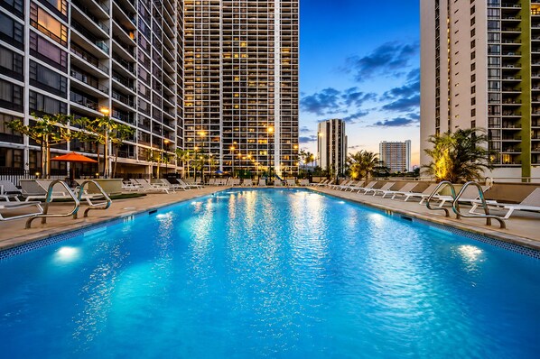 A swimming pool with lounge chairs, surrounded by high-rise buildings.