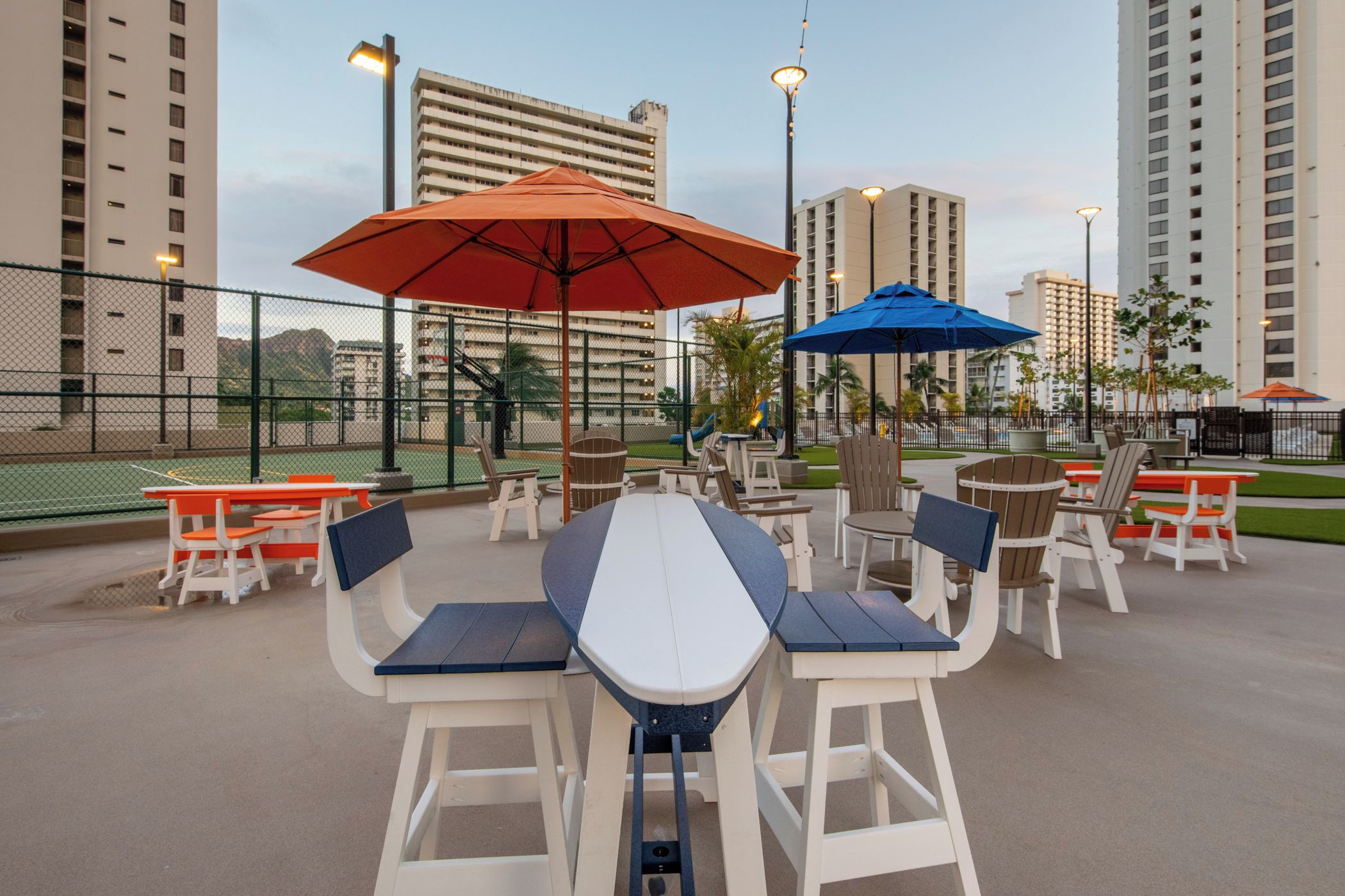 Outdoor seating with tables and chairs, umbrellas, and a fence.