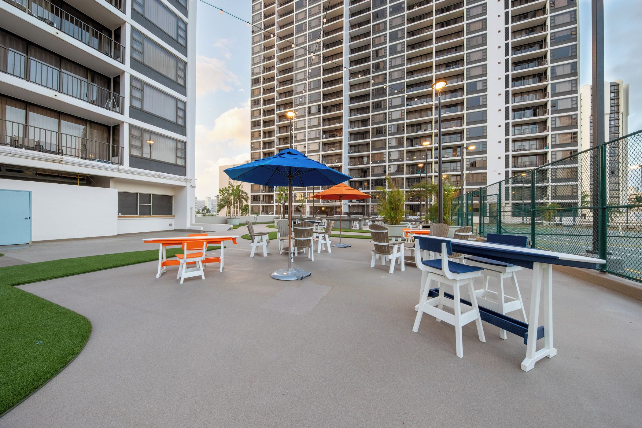 Un espace extérieur aménagé en terrasse, avec des tables et des chaises, entouré d’un immeuble de grande hauteur.