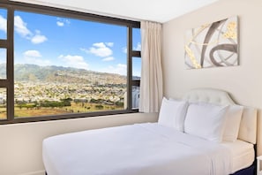 Een hotelkamer met een groot raam met uitzicht op een stadsbeeld en bergen.