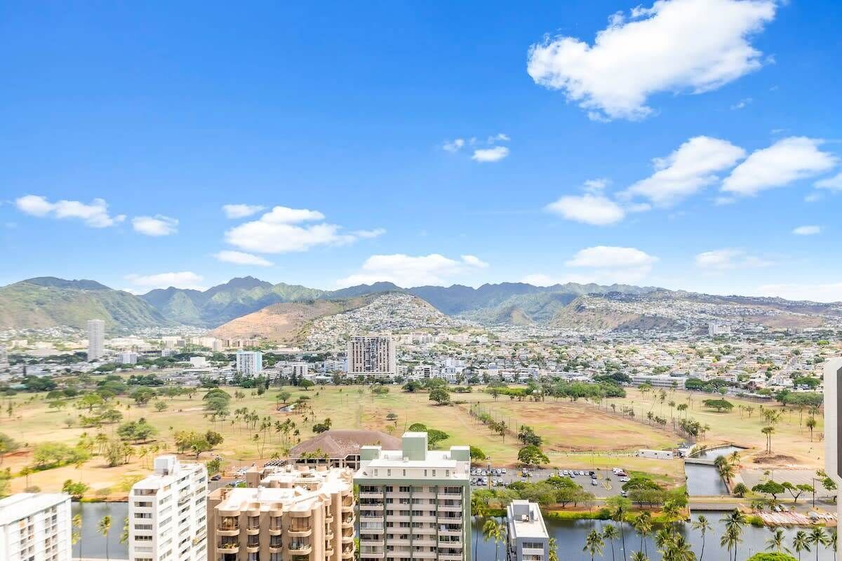 Vista de un paisaje urbano con montañas, edificios residenciales y una zona verde.