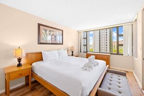 A hotel room with a large bed, a window with a view of buildings, a framed picture on the wall, and a bedside table with a lamp. - Ocean & Diamond Head view 19th FL w/ Free Parking (Honolulu)