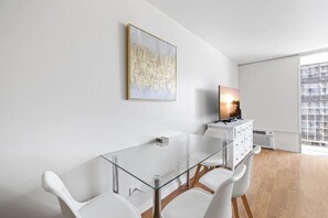 A modern living room with a glass dining table, white chairs, a white cabinet, and a painting on the wall. - Partial ocean view, 13th FL, Renovated, Free Parking (Honolulu)