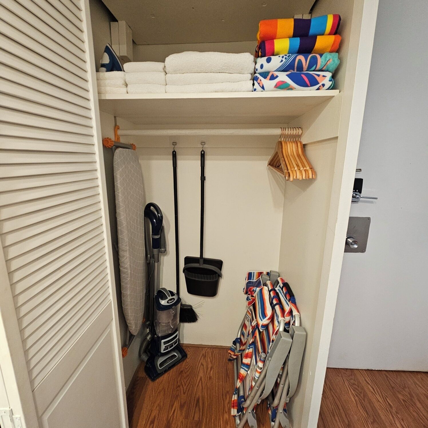 A compact storage area with a shelf holding folded towels and a vacuum cleaner.