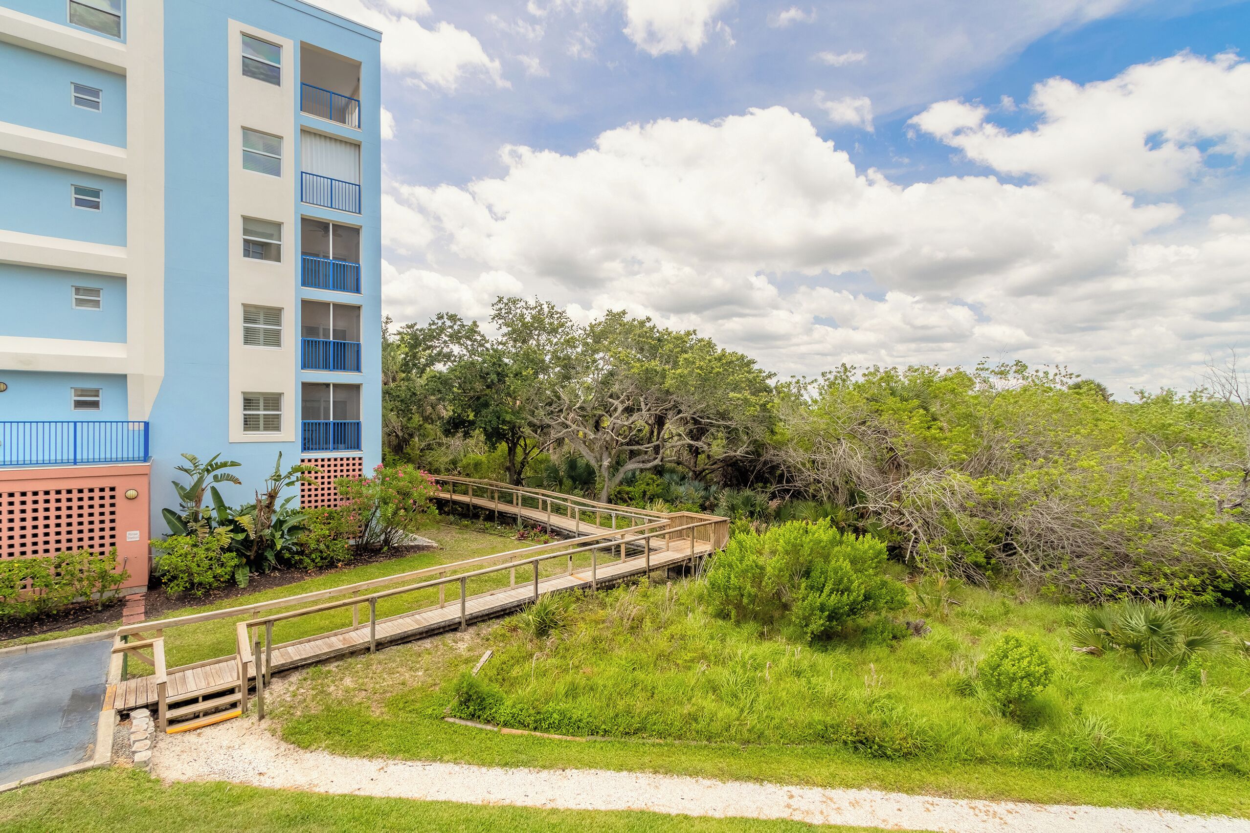 A multi-story building with balconies, a wooden walkway, and surrounding greenery.