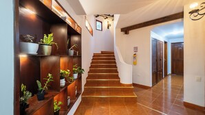 Una escalera con barandilla de madera, flanqueada por estantes con plantas en macetas, que conduce a una puerta en la parte superior.