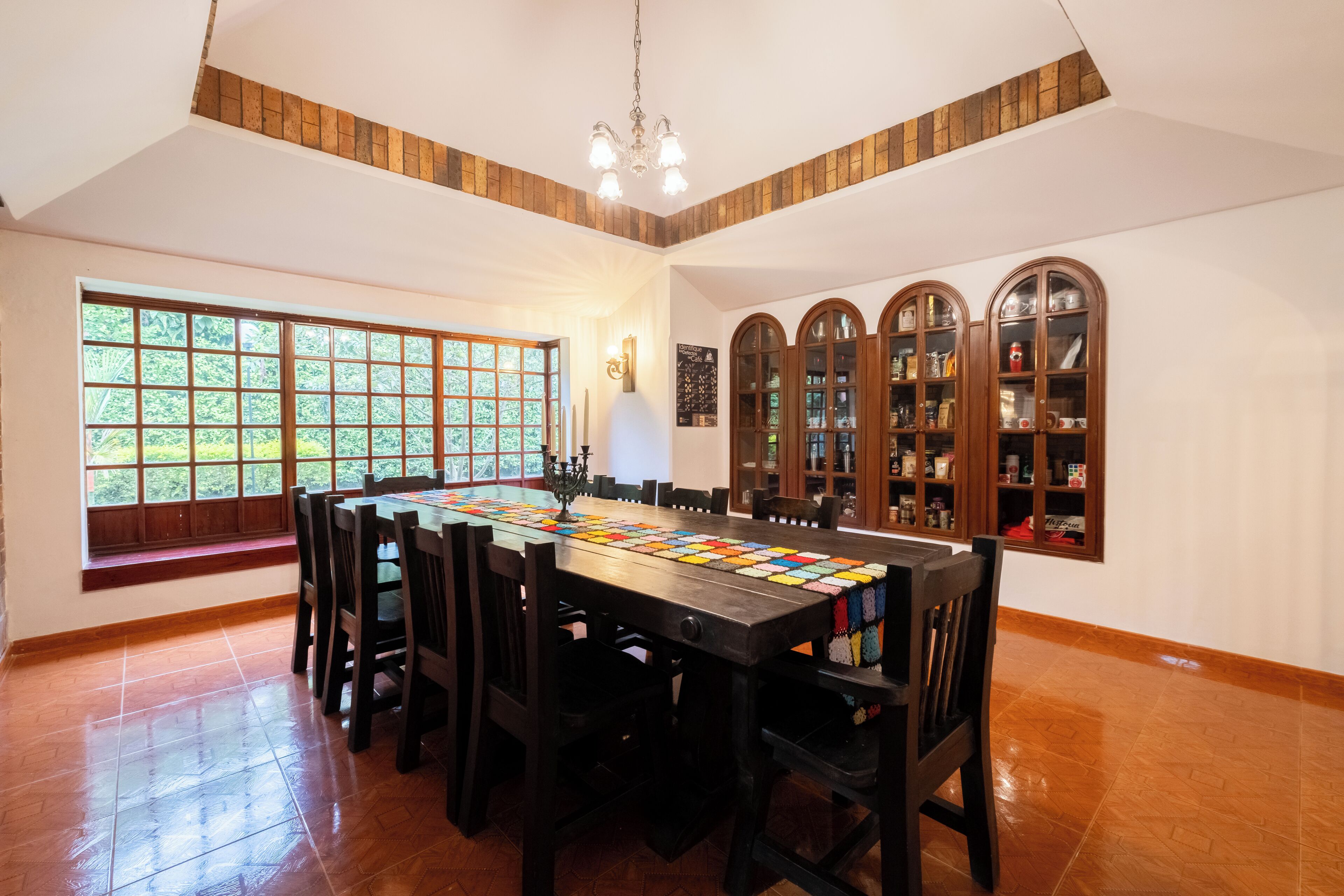 A dining area with a long table, multiple chairs, a chandelier, and built-in bookshelves.
