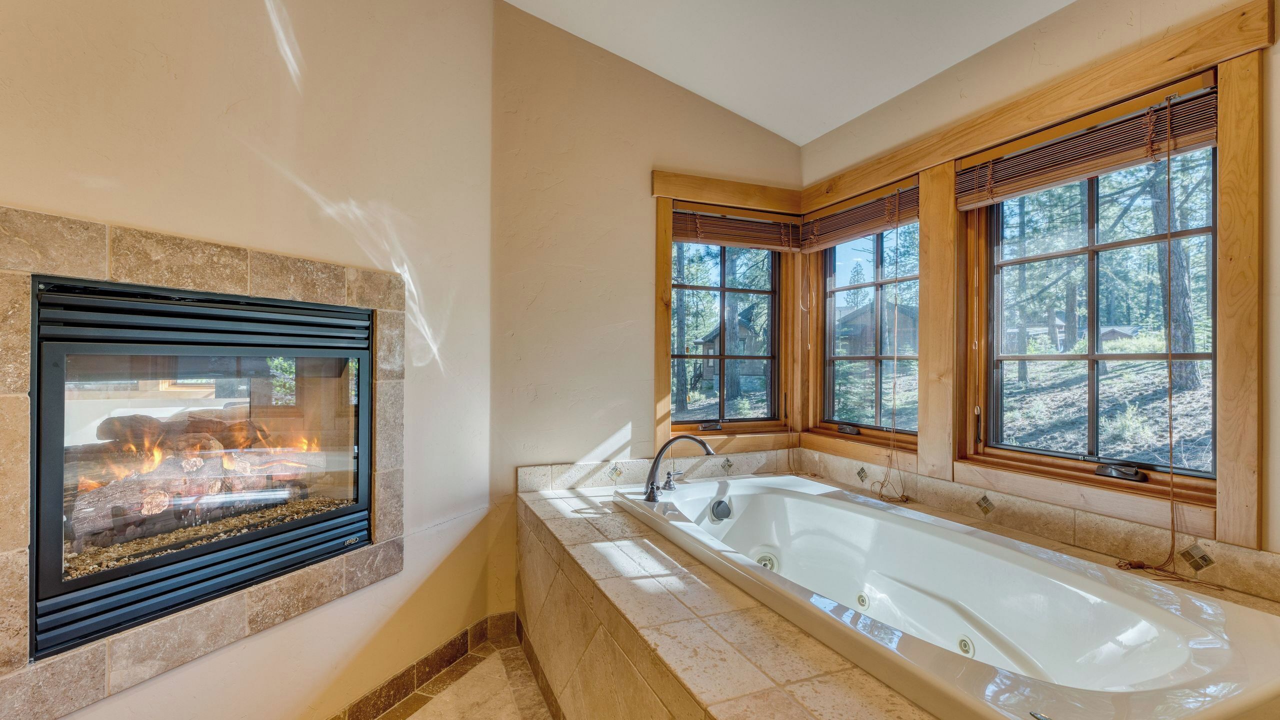 A bathroom with a large bathtub, a fireplace, and windows with a forest view.