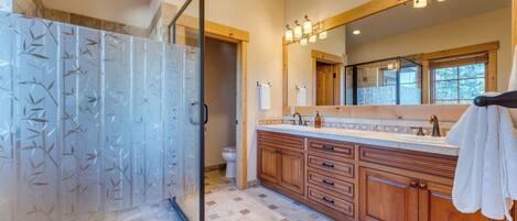 A bathroom with a glass shower enclosure, wooden cabinets, a large mirror, and a window.