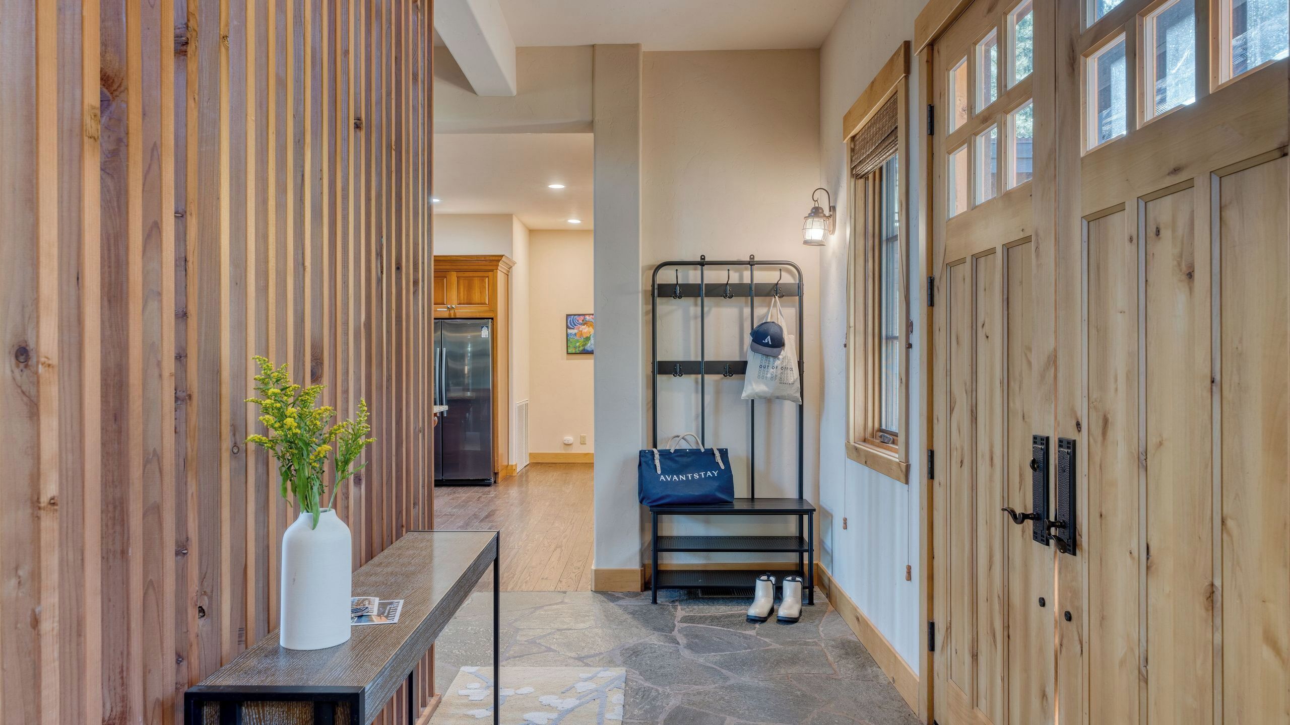 A hallway with wooden paneling, a stone-tiled floor, a metal bench, and a coat rack with bags.