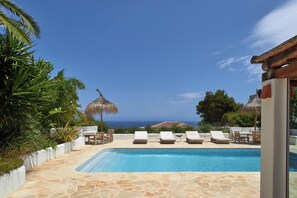 A pool with lounge chairs, a thatched umbrella, and a view of the sea.