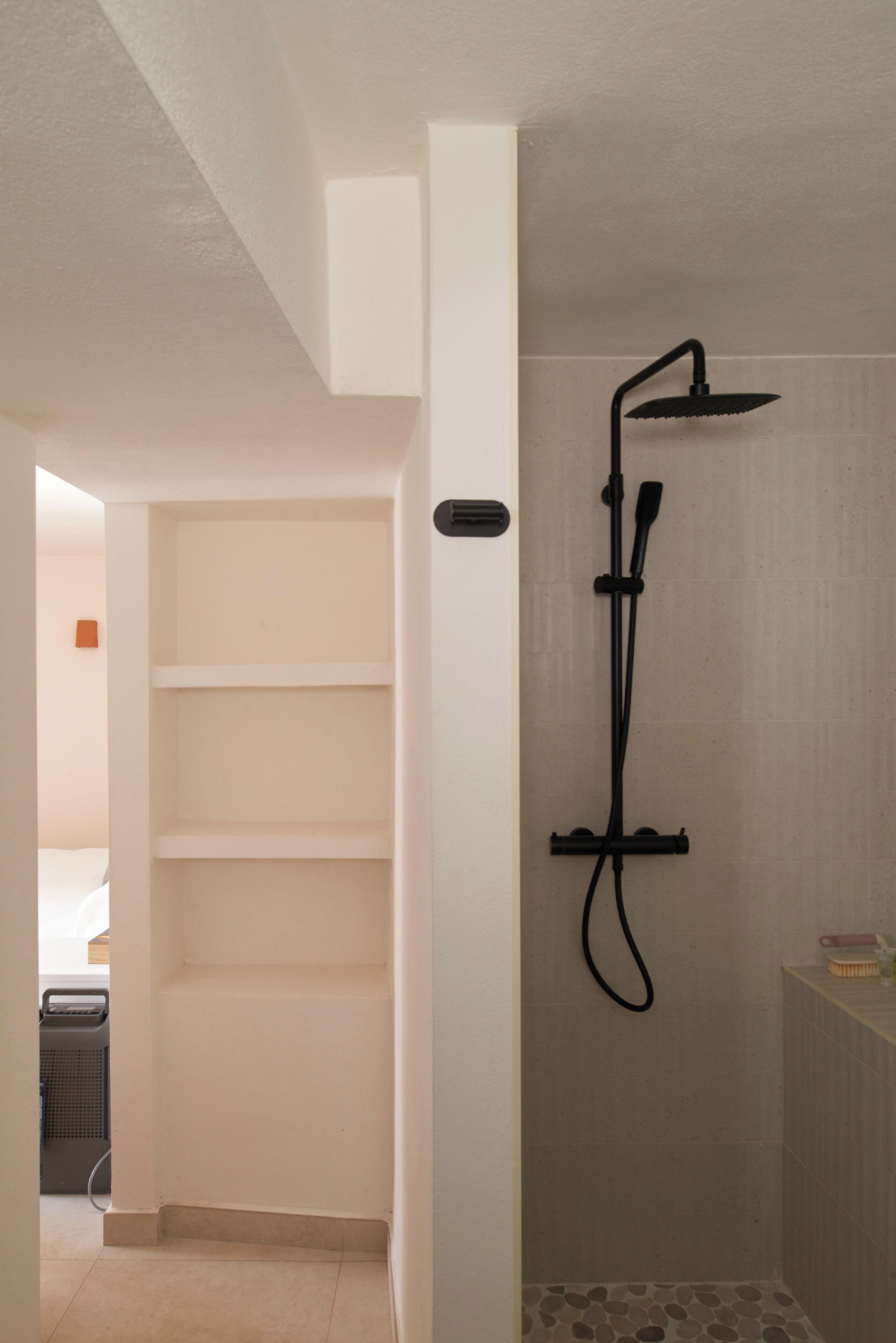 A shower with a handheld showerhead, a wall-mounted control panel, and tiled walls.