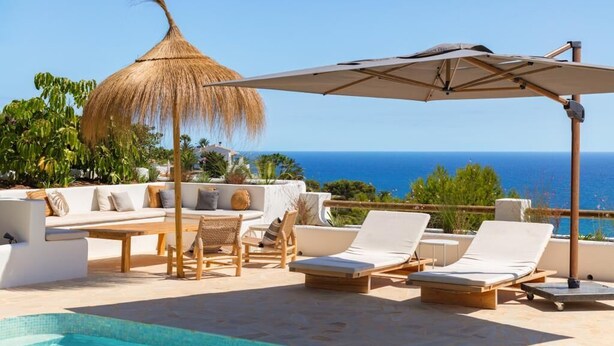 Un espace aménagé au bord de la piscine, avec des chaises longues, un parasol en chaume et une vue sur l’océan.