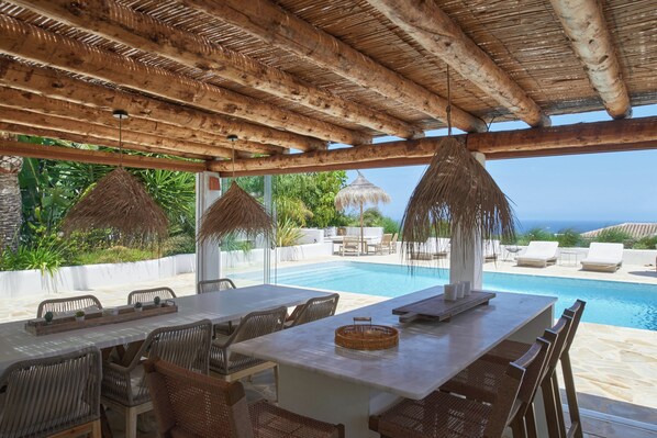 Un espace aménagé au bord de la piscine, doté d’une pergola en bois, de mobilier en osier et offrant une vue sur l’océan.