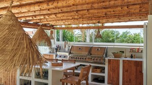 Une cuisine extérieure dotée d’un sol en pierre, d’un plafond en bois et de meubles en osier.