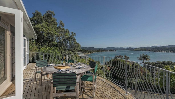 Eine Terrasse mit Esstisch, mit Blick auf ein Gewässer und Hügel.