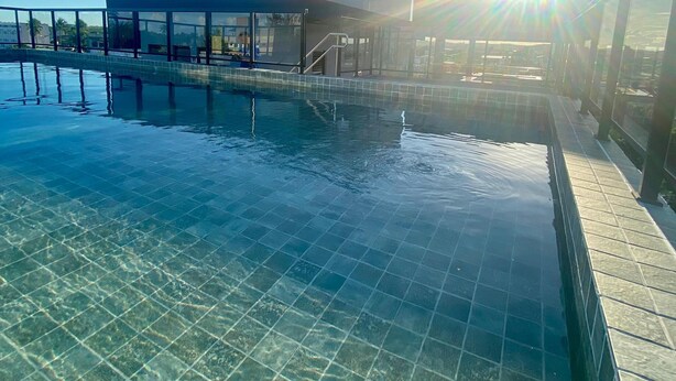 Una piscina infinita al aire libre con agua azul cristalina, un puente de cristal y un edificio moderno al fondo.