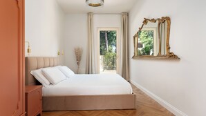 A bedroom with a bed, a nightstand, a mirror, and a view of greenery outside. - Casa Amare 4+2, Emma Villas (Camaiore)