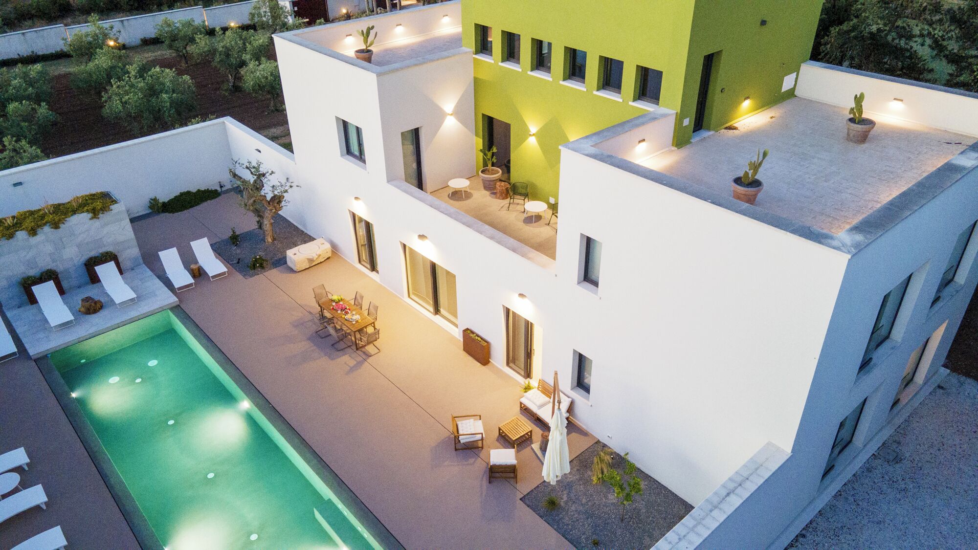 Un edificio moderno de dos pisos con piscina, asientos al aire libre y plantas en macetas.