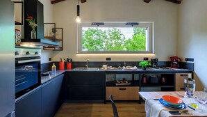 Een compacte keuken met een inbouwoven, een spoelbak en een raam met uitzicht op groen.
