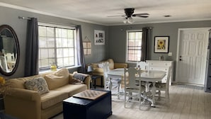Una sala de estar con un sofá color beige, una mesa de centro, una mesa de comedor con sillas y un ventilador de techo.