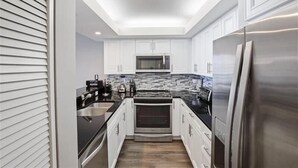 A modern kitchen with white cabinets, stainless steel appliances, and a black countertop. - Come enjoy sun and sand in Naples luxury-WS0803 (Naples)
