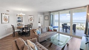 A spacious living area with a sofa, dining table, and chairs, a balcony with a view of the sea, and artwork on the walls. - Come enjoy sun and sand in Naples luxury-WS0803 (Naples)