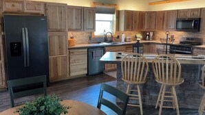 A modern kitchen with wooden cabinets, a stainless steel refrigerator, a microwave, and a stove. There is a dining area with a table and chairs. - Secluded and spacious Barndominium close to 2 Ski Resorts and many attractions! (Factoryville)