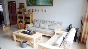 Uma sala de estar com um sofá, uma mesa de centro, uma poltrona, uma estante de livros e um quadro na parede.