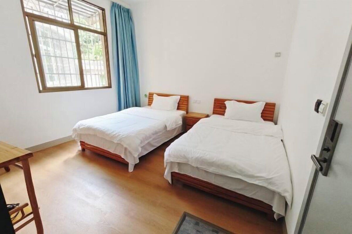 Una habitación con dos camas individuales, una mesa de madera y una ventana con cortinas.