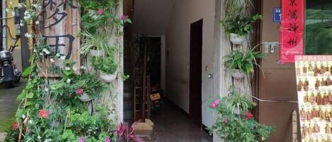 A doorway with a wooden sign, potted plants, and a red banner.