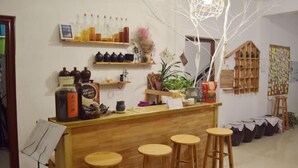 Um espaço de bar acolhedor, com banquetas de madeira, prateleiras com garrafas e objetos decorativos, e uma luminária pendente.