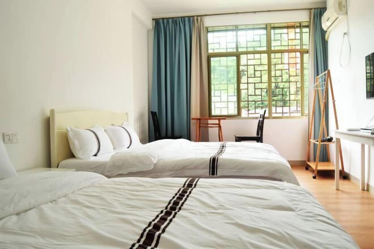 Una habitación de hotel con dos camas, un escritorio y una silla cerca de una ventana con cortinas.