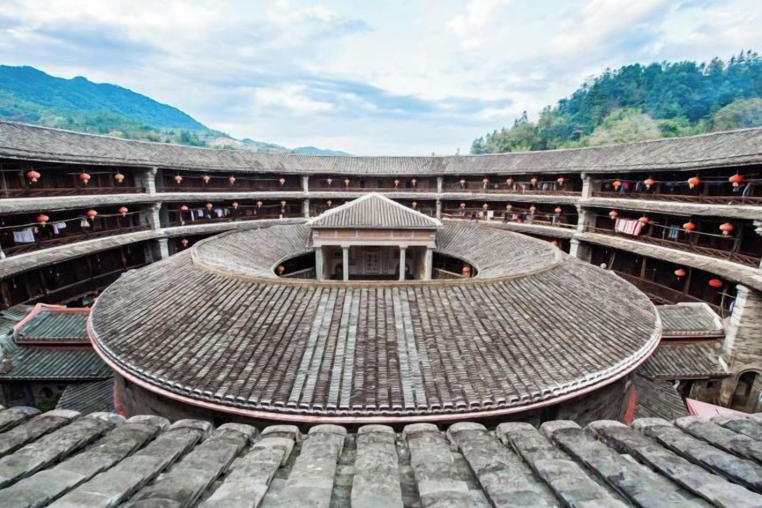 Un patio circular tradicional con asientos escalonados y un pabellón central, rodeado por una valla de madera y con montañas al fondo.