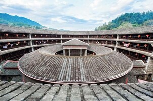 Um pátio circular tradicional com assentos em terraços e um pavilhão central, cercado por uma cerca de madeira e com montanhas ao fundo.