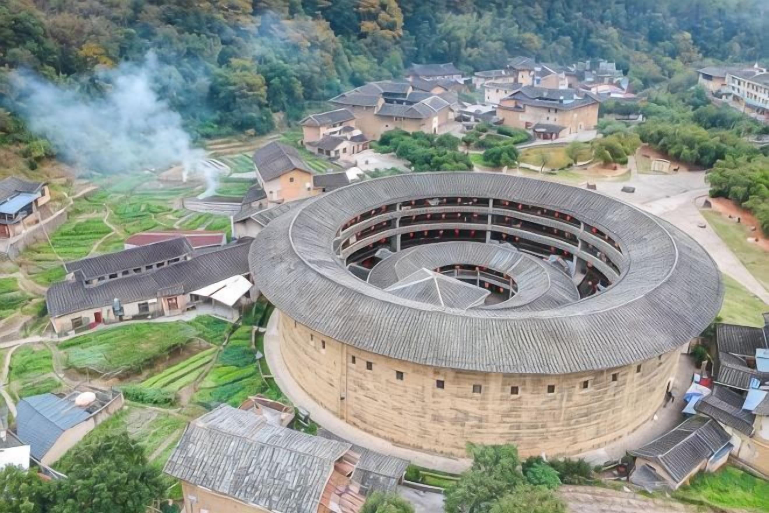 Un edificio circular con varios pisos, rodeado de casas residenciales y vegetación.