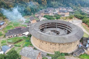 Un edificio circular con varios pisos, rodeado de casas residenciales y vegetación.