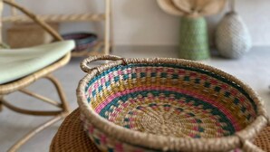 A wicker basket with a colorful woven pattern, a wicker chair, and a wall-mounted fan in a room with a neutral color scheme. - Rue Rooms (Fethiye)