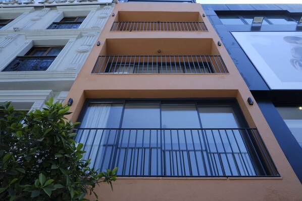 A multi-story building with balconies, large windows, and a tree in the foreground. - Rue Rooms (Fethiye)